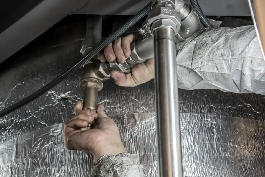 Technician servicing drain and trap fittings under a commercial kitchen sink